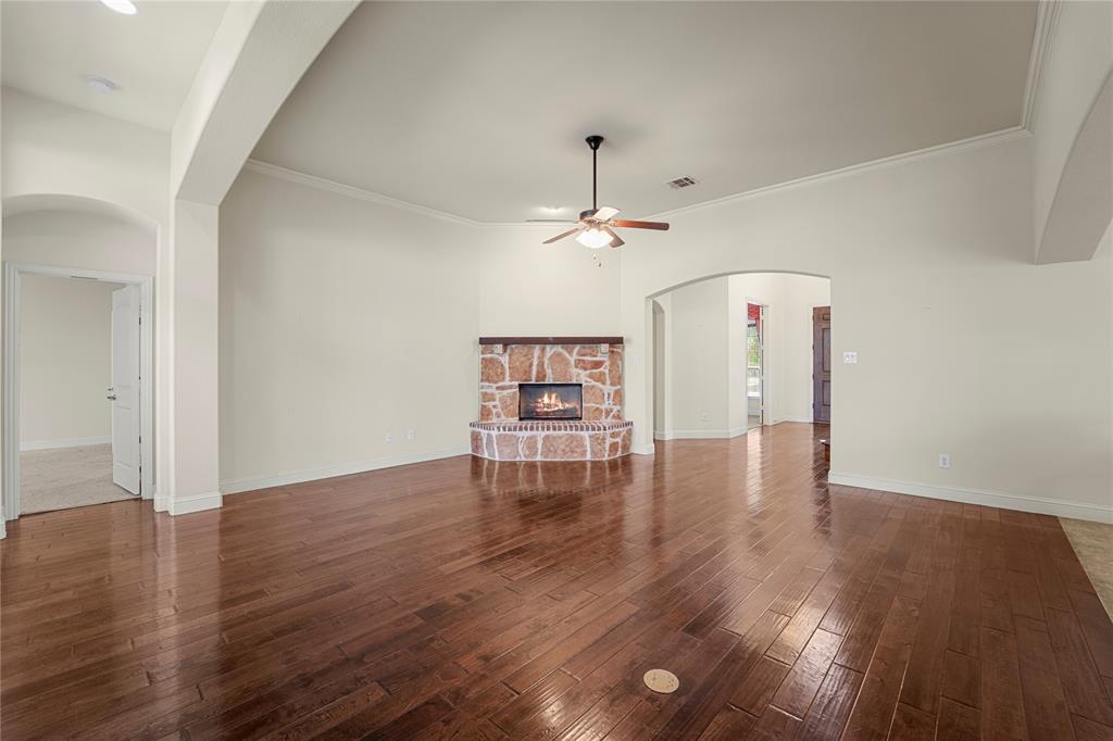 Living area featuring high ceilings, wood-finish flooring, corner stone fireplace with a timber mantel, and a ceiling fan