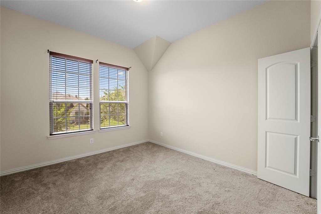 Vaulted ceiling room featuring neutral carpeting, two dual-pane windows with horizontal blinds, and a solid-core interior door
