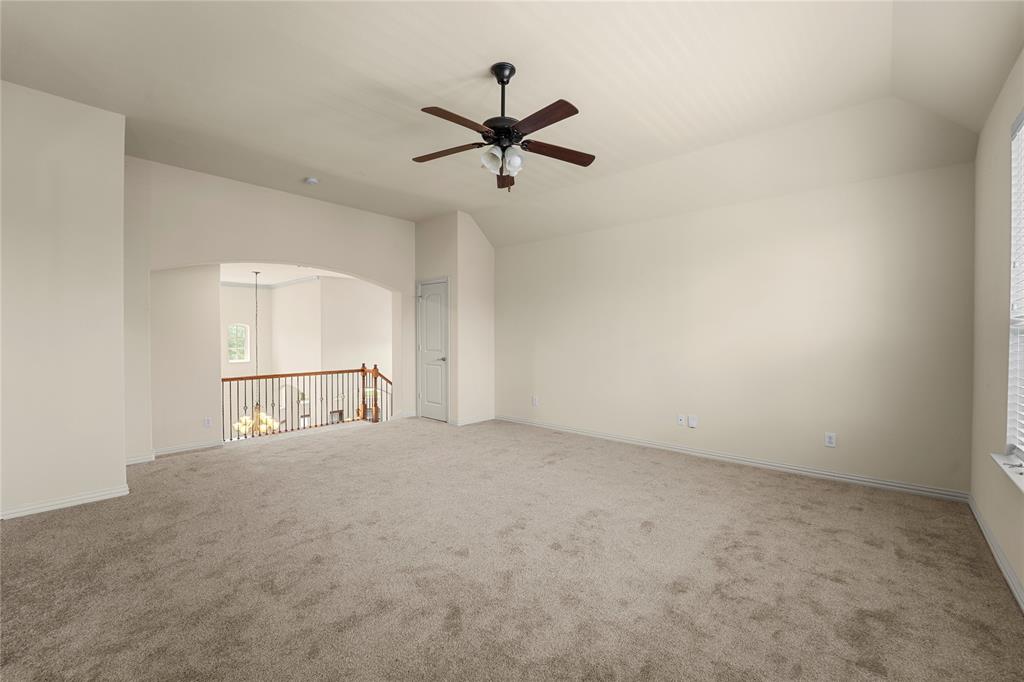 Vaulted ceiling, carpeted flooring, centrally mounted ceiling fan with integrated lighting, and wooden baluster railing