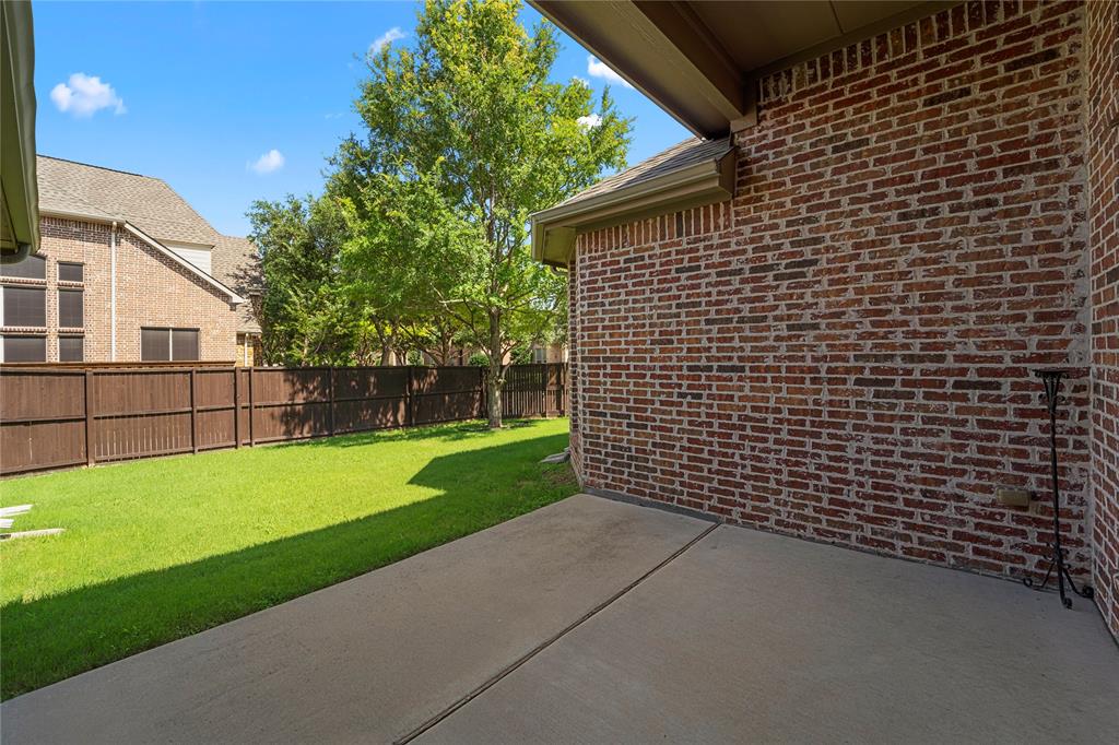 Covered concrete patio featuring brick exterior walls and a fenced backyard with a lawn