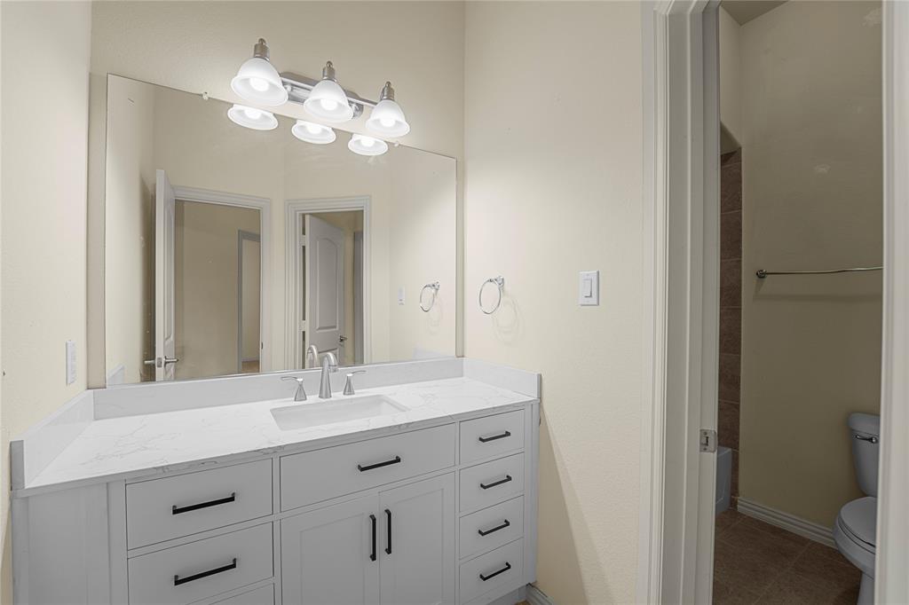 White vanity featuring an integrated rectangular sink, light stone-patterned countertop, matte black hardware, and an expansive wall-mounted mirror with a three-light fixture