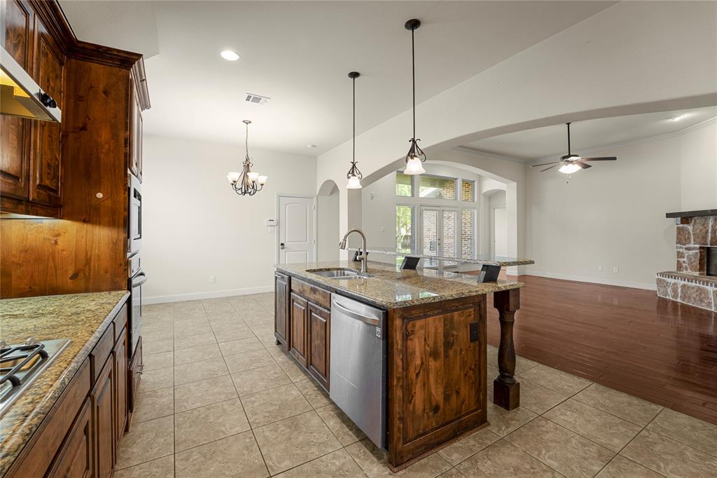 Kitchen featuring stained wood cabinetry, stone-surface countertops, central island with stainless steel appliances, dual-pendant lighting, and ceramic tile flooring
