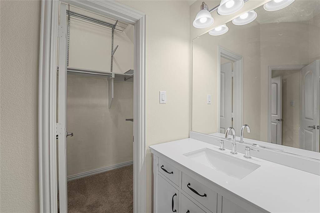 White vanity with stone-composite countertop, undermount sink, chrome fixtures, full-width vanity mirror, and built-in closet shelving