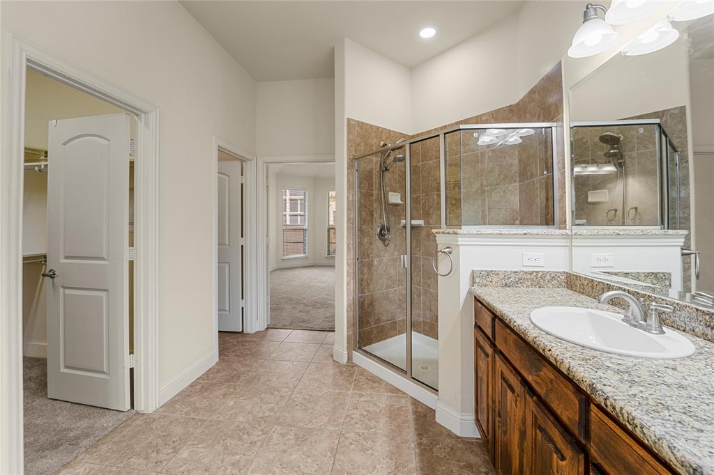 Bathroom featuring a walk-in shower with tile surround, stone-composite countertop with an integrated basin, stained wood cabinetry, and large-format tile flooring