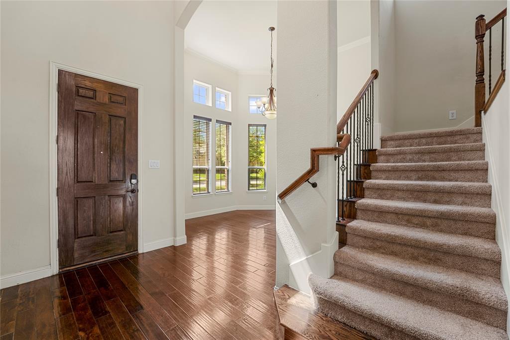 Foyer featuring wood-finish flooring, a solid wood-panel entry door, a multi-paneled window grouping, and a staircase with wrought-iron balusters and a polished wood handrail