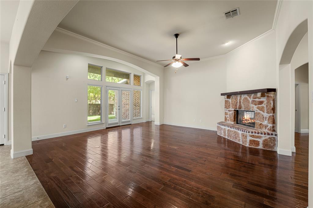 Spacious living area featuring wood-finish flooring, vaulted ceilings, a stone-accented fireplace with a wood mantel, and large windows with integrated glass doors
