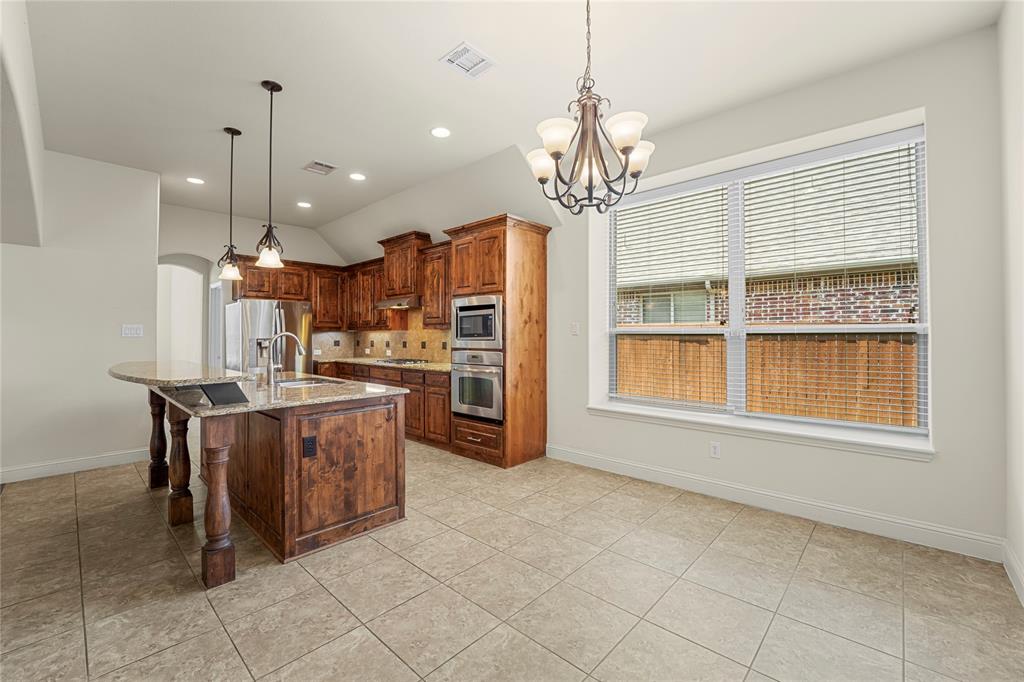 Kitchen featuring wood cabinetry, stone-surface countertops, tile flooring, built-in wall oven and microwave, and multi-light hanging fixtures