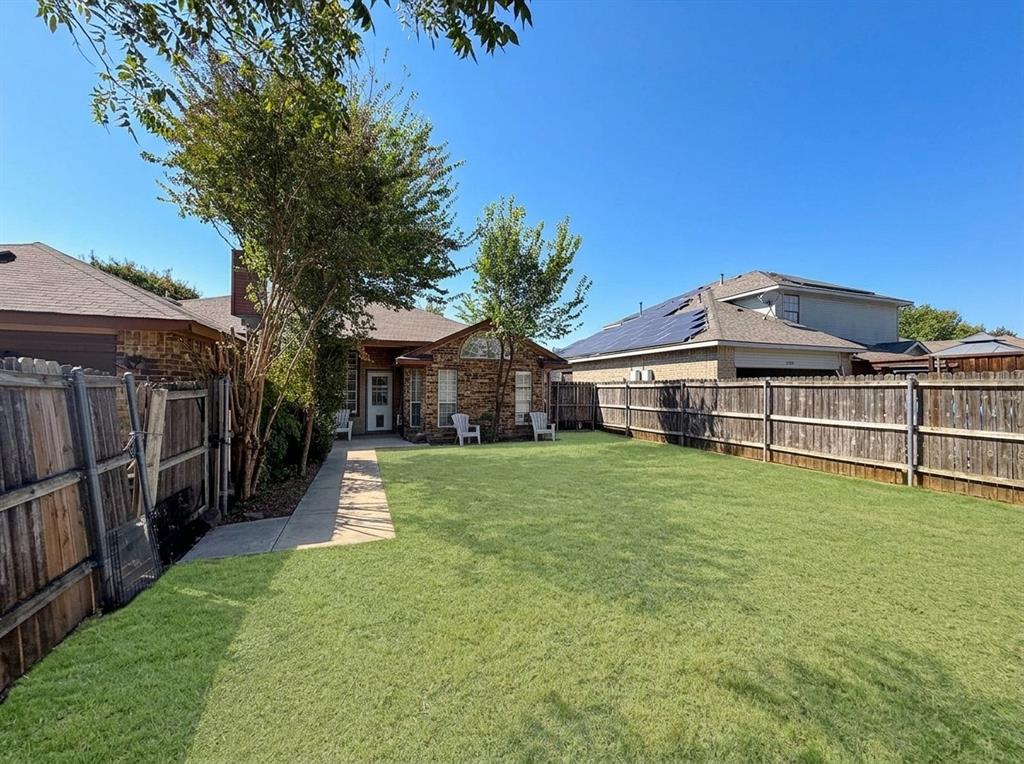 Fenced backyard featuring a manicured lawn, mature trees, and a concrete pathway