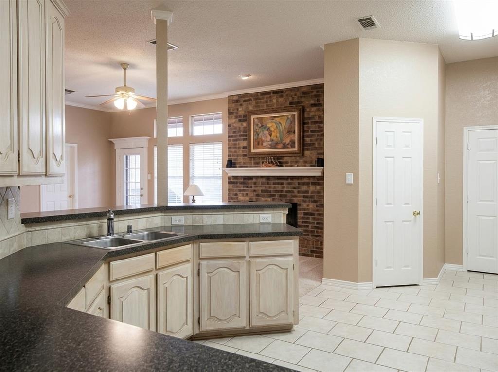 Kitchen featuring off-white cabinetry, dark countertops, a double-basin stainless steel sink, and tile flooring, with a brick fireplace surround