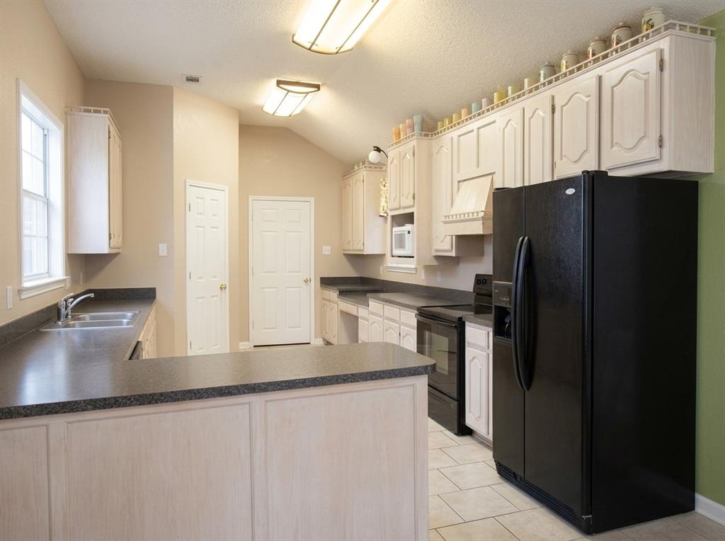 Kitchen featuring light-toned cabinetry, dual-basin stainless steel sink, dark solid-surface countertops, vaulted ceiling, and tile flooring