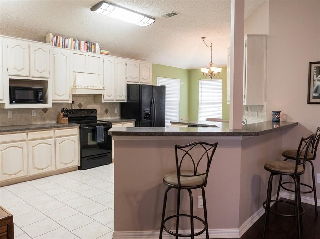 Kitchen featuring white raised-panel cabinetry, stone-composite countertops, tile backsplash, built-in microwave, and breakfast bar