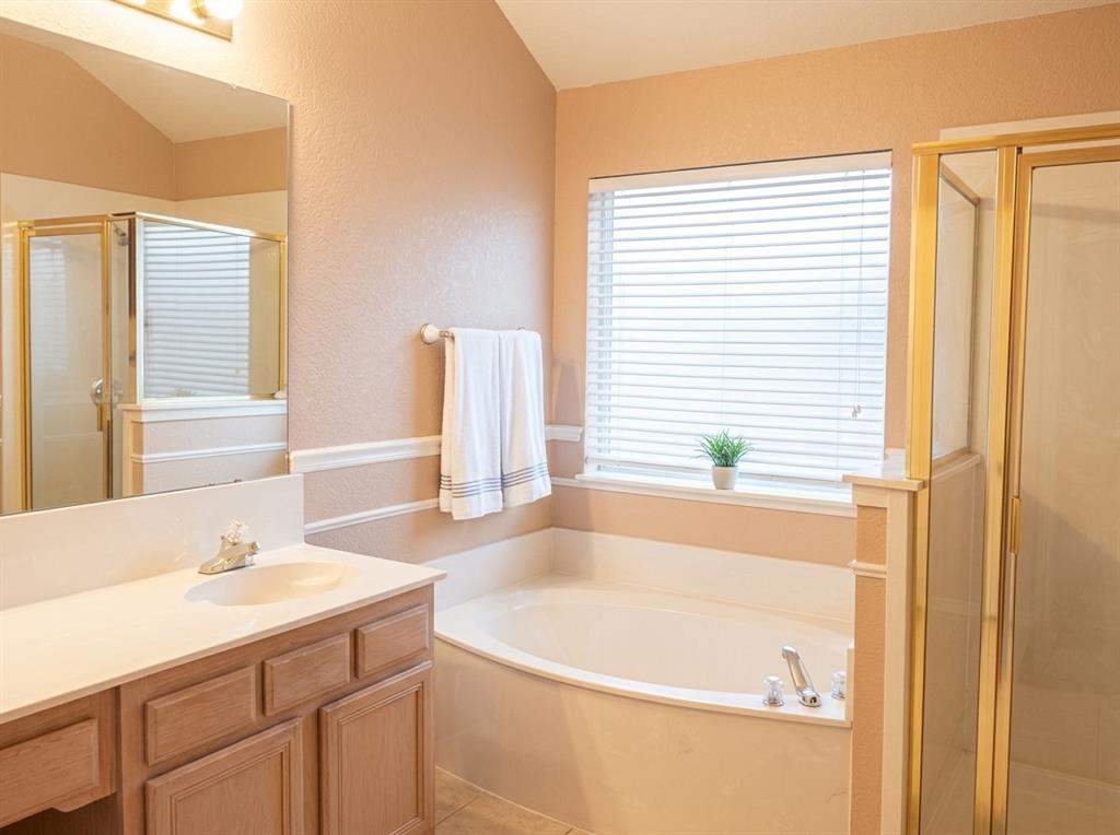 Bathroom featuring a wood vanity with a solid-surface countertop, an integrated sink, a built-in soaking tub, a separate shower enclosure with a frame, and a large wall-mounted mirror