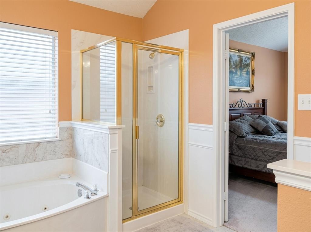 Jetted soaking tub with tile surround, glass-enclosed shower with gold-tone frame, and white wainscoting