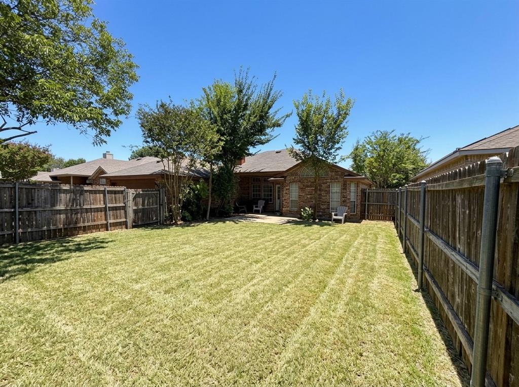 Backyard featuring a manicured lawn, masonry exterior, concrete patio, wood-plank fencing, and mature trees