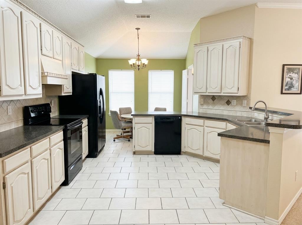 Kitchen featuring white raised-panel cabinetry, dark countertops, a vaulted ceiling, tiled flooring, and a multi-light chandelier