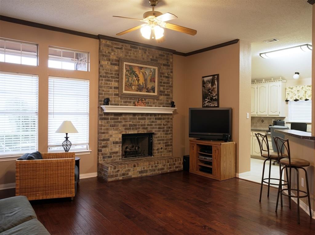 Floor-to-ceiling brick fireplace with a custom mantel, wood-finish flooring, and crown molding