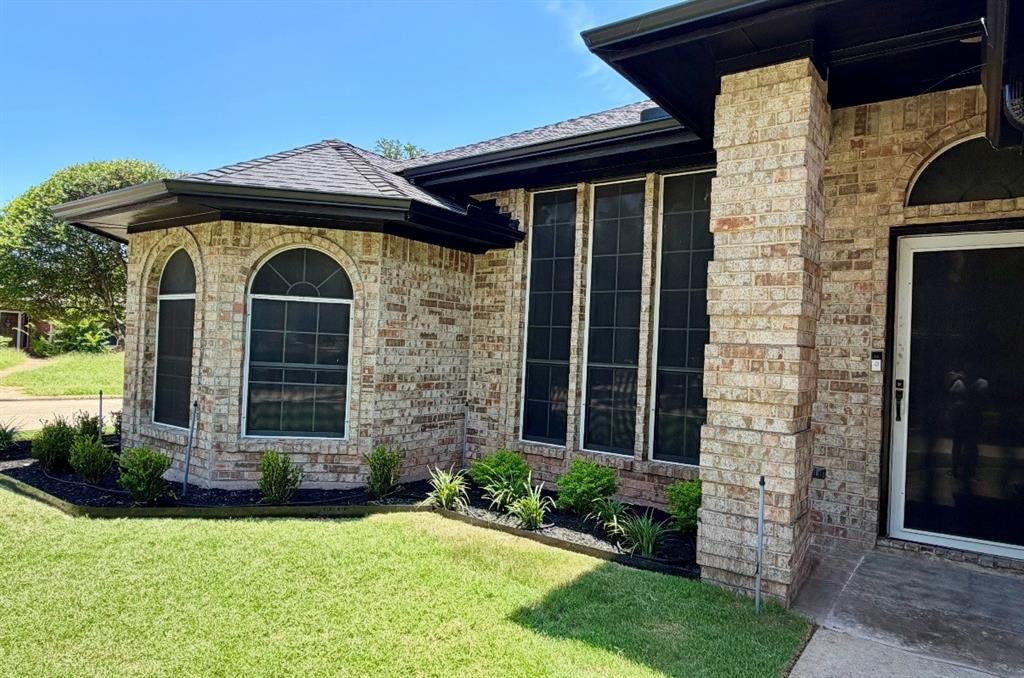 Exterior brick facade with stone-textured pillar, architectural roof shingles, arched windows, and dark metal trim framing