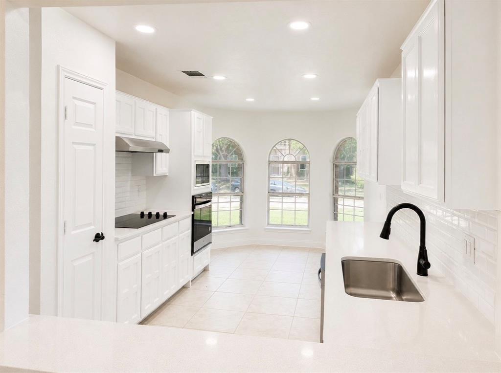Kitchen featuring white cabinetry, quartz countertops, subway tile backsplash, stainless steel appliances, and arched windows