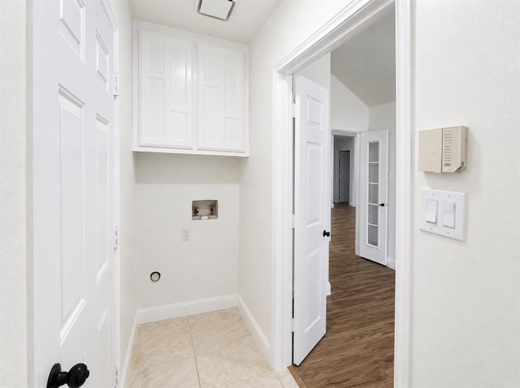 Utility area featuring white upper cabinetry, tiled flooring, wood-finish flooring in the exterior space, and multi-panel doors with matte black hardware