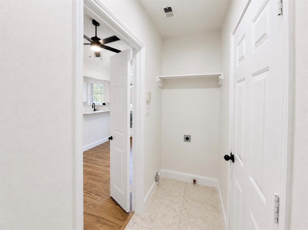 Dedicated utility area featuring tile flooring, a wall-mounted storage shelf, and crisp white paneled doors with matte black hardware
