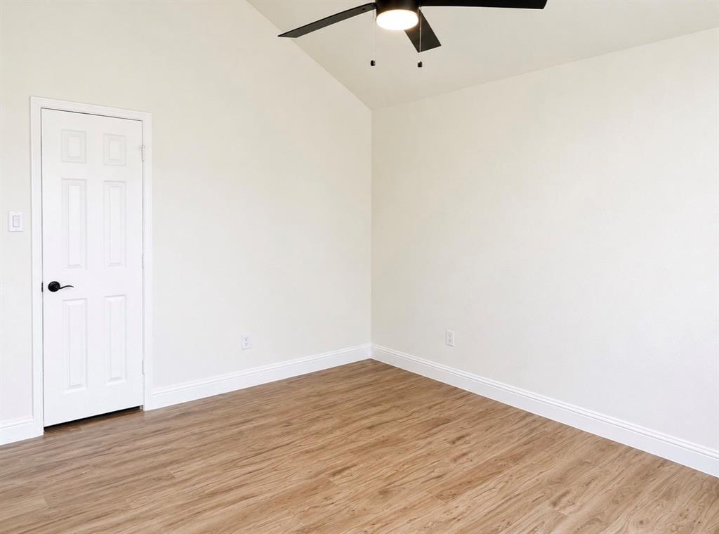Vaulted ceiling featuring a central black ceiling fan with an integrated light fixture, complemented by wood-finish flooring and a white six-panel interior door with matte black hardware