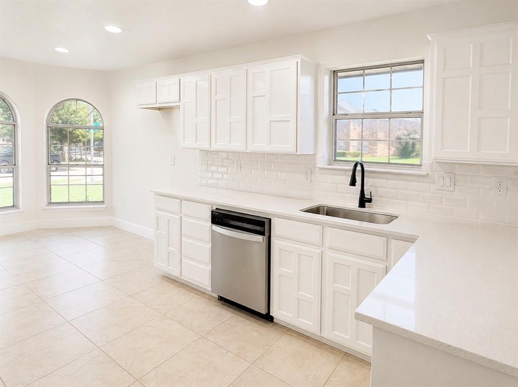Kitchen featuring white cabinetry, subway tile backsplash, light-toned countertops, stainless steel dishwasher, and arched windows