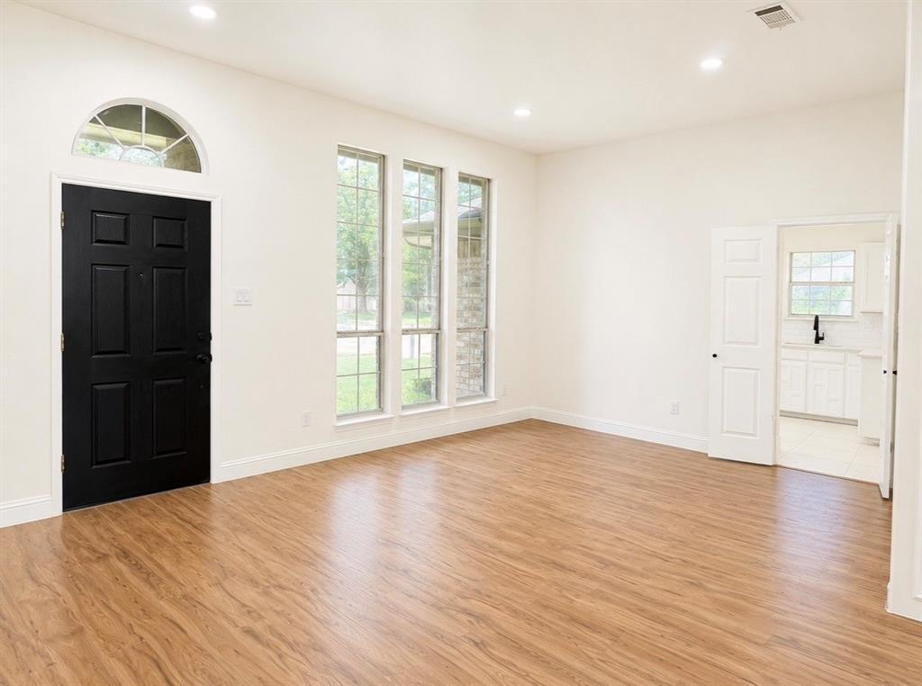 Interior room featuring wood-finish flooring, recessed lighting, a contrasting black entry door with an arched transom window, and triple vertical windows