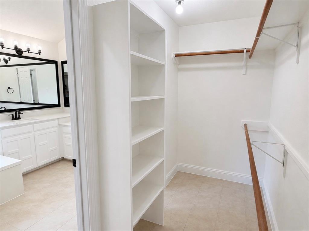 Walk-in closet featuring floor-to-ceiling built-in shelving and dual-tier wooden hanging rods, accompanied by a bathroom vanity with a black-framed mirror, white cabinetry, and matte black hardware
