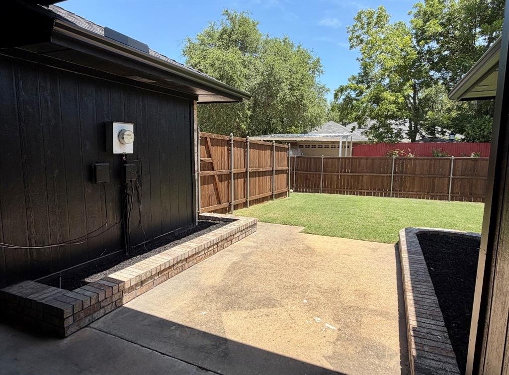 Concrete patio featuring dual raised brick planters, enclosed by a wood privacy fence and expansive lawn