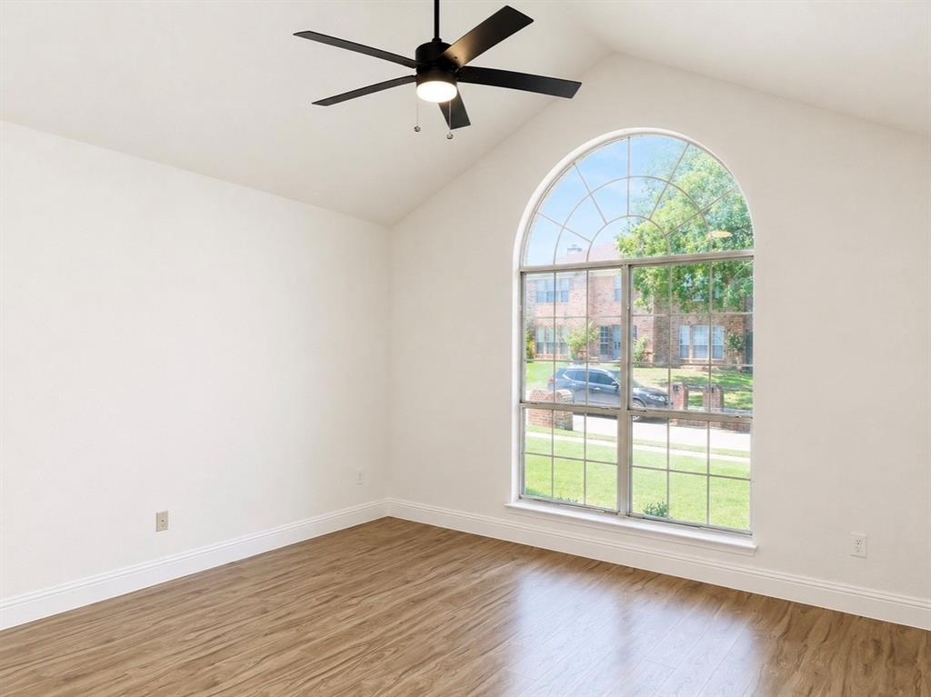 Vaulted ceiling with an arched window, wood-finish flooring, and a matte black ceiling fan with integrated lighting