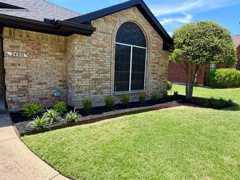 Brick exterior featuring a gabled roofline, arched window with decorative grille, and landscaped garden beds with dark mulch
