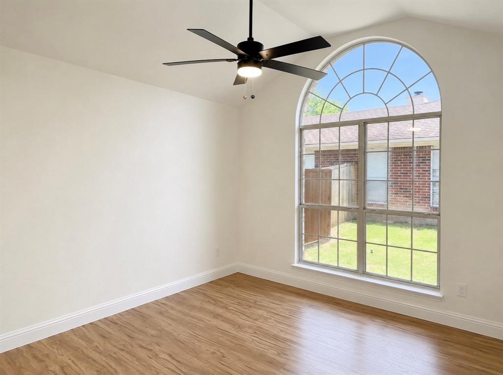 Vaulted ceilings, wood-finish flooring, large arched window with muntin detailing, and a multi-blade ceiling fan with integrated lighting