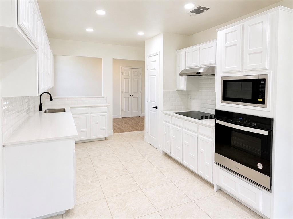 Kitchen featuring white cabinetry with geometric panel detailing, solid surface countertops, a white subway tile backsplash, recessed lighting, and a built-in stainless steel wall oven and microwave combination