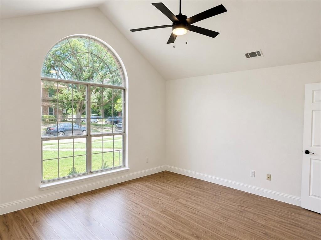 Vaulted ceiling featuring a matte black ceiling fan, wood-finish flooring, and an arched window
