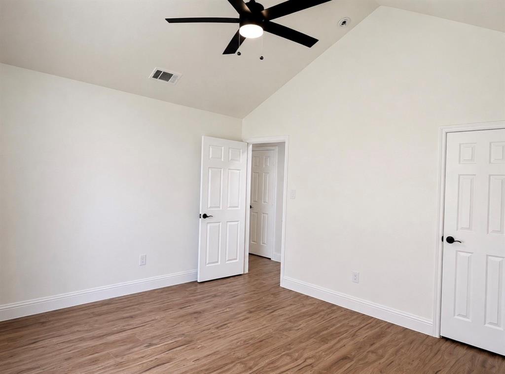 Vaulted ceilings featuring a matte black finish ceiling fan, wood-finish flooring, and six-panel interior doors with matte black hardware