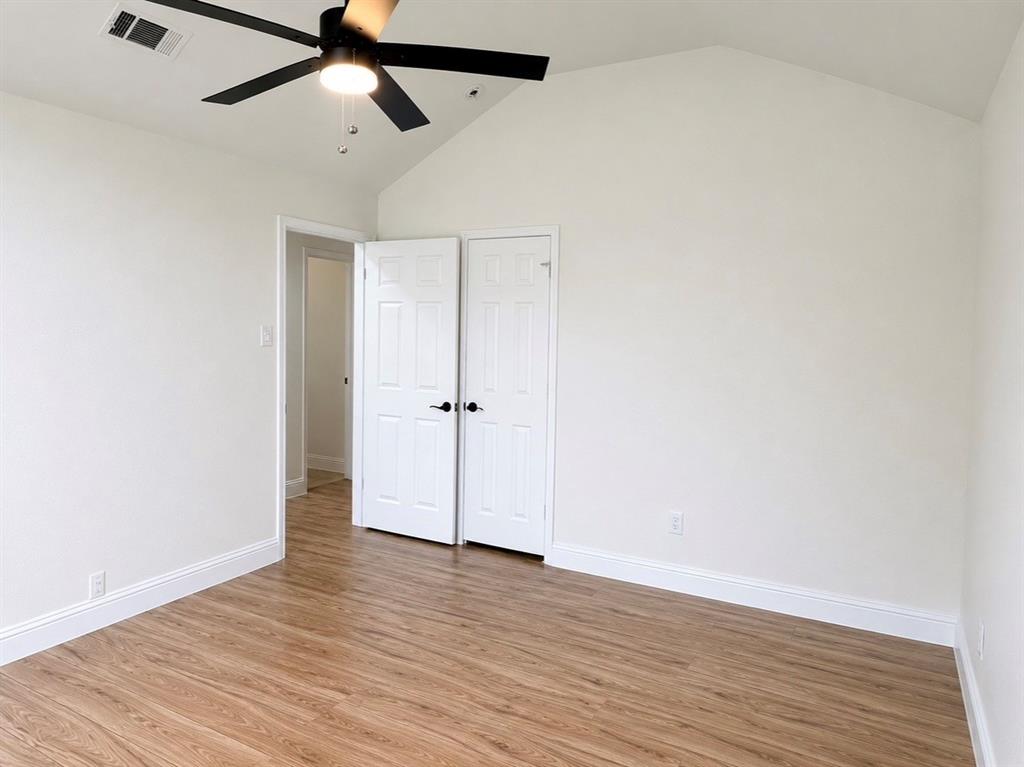 Vaulted ceiling with a matte black four-blade ceiling fan, wood-finish flooring, and white paneled closet doors with matte black hardware