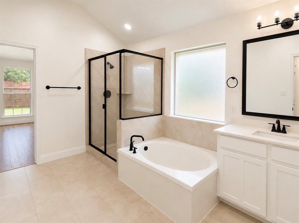 Bathroom featuring a soaking tub, separate glass-enclosed shower with matte black fixtures, vanity with quartz countertop, and framed mirror