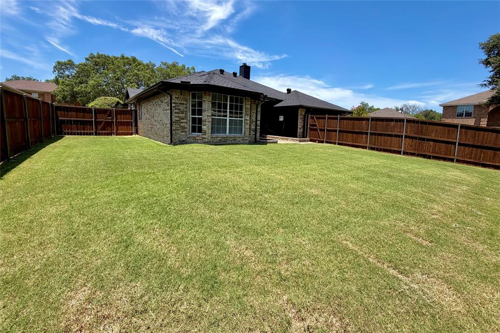 Expansive backyard featuring a manicured lawn, full-perimeter wood fencing, and brick exterior construction