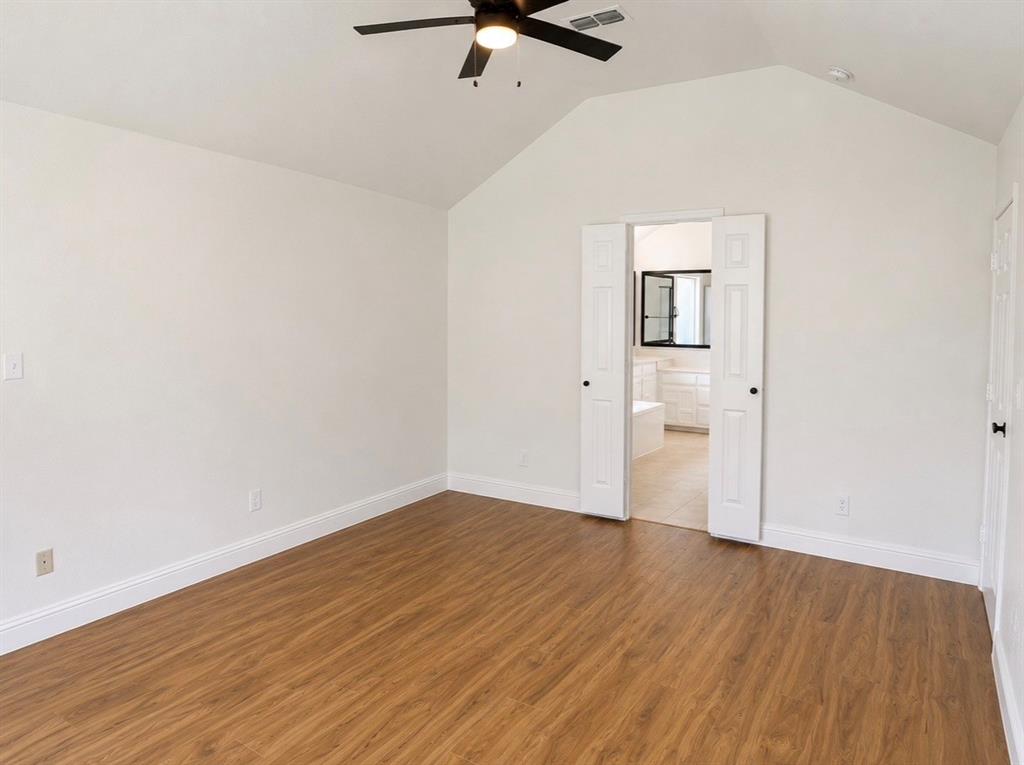 Vaulted ceiling featuring a central lighted ceiling fan, wood-finish flooring, and white paneled double doors