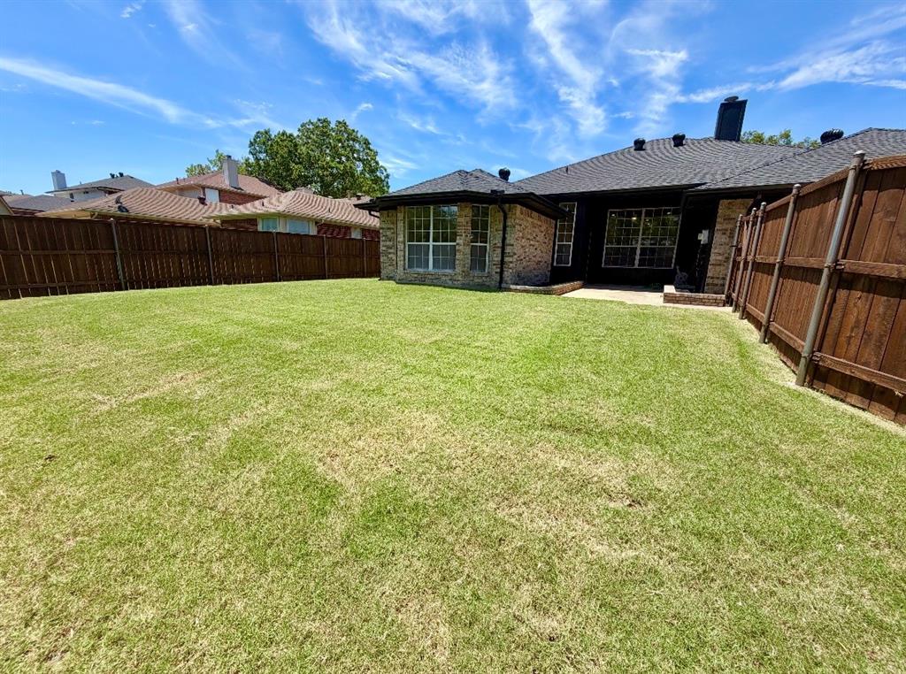 Expansive backyard featuring a sod lawn, perimeter wood privacy fencing, and exterior masonry detailing