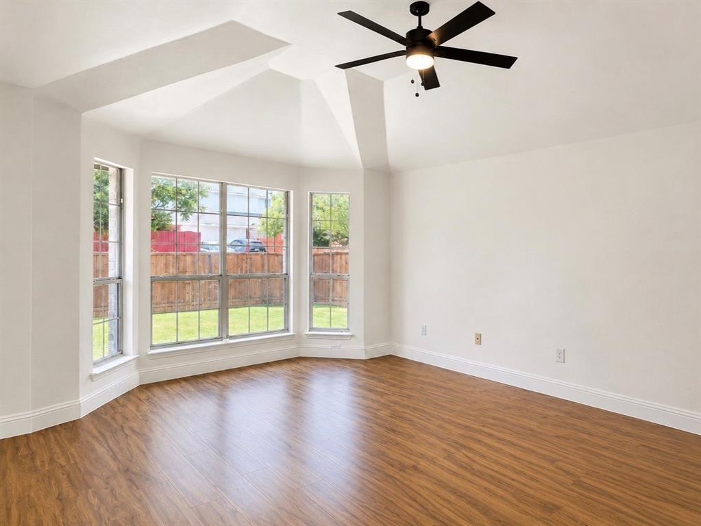 Vaulted ceiling featuring a central matte black ceiling fan with integrated lighting, wood-finish flooring, and a triple-pane bay window assembly