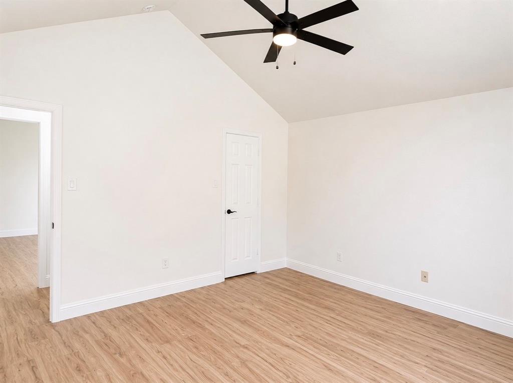 Vaulted ceiling featuring a central matte black six-blade ceiling fan with integrated lighting and wood-finish flooring