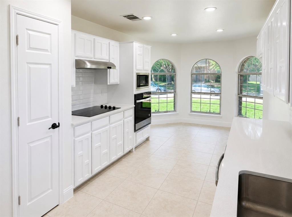 Kitchen featuring crisp white shaker-style cabinetry, quartz countertops, subway tile backsplash, stainless steel built-in appliances, and arched windows