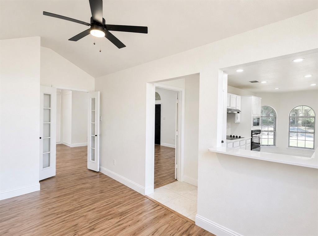 Vaulted ceilings featuring a matte black finish ceiling fan, white French doors, wood-finish flooring, and a kitchen pass-through window with a white countertop