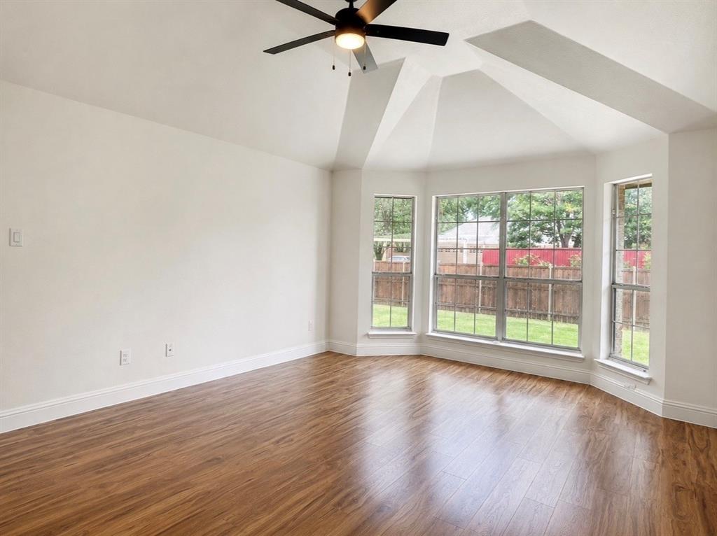 Vaulted ceilings, wood-finish flooring, bay windows, and a matte black ceiling fan with integrated lighting