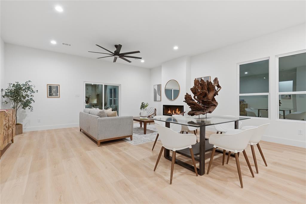 Open-concept area featuring high ceilings, wood-finish flooring, a wall-mounted fireplace, recessed lighting, and a multi-blade ceiling fan