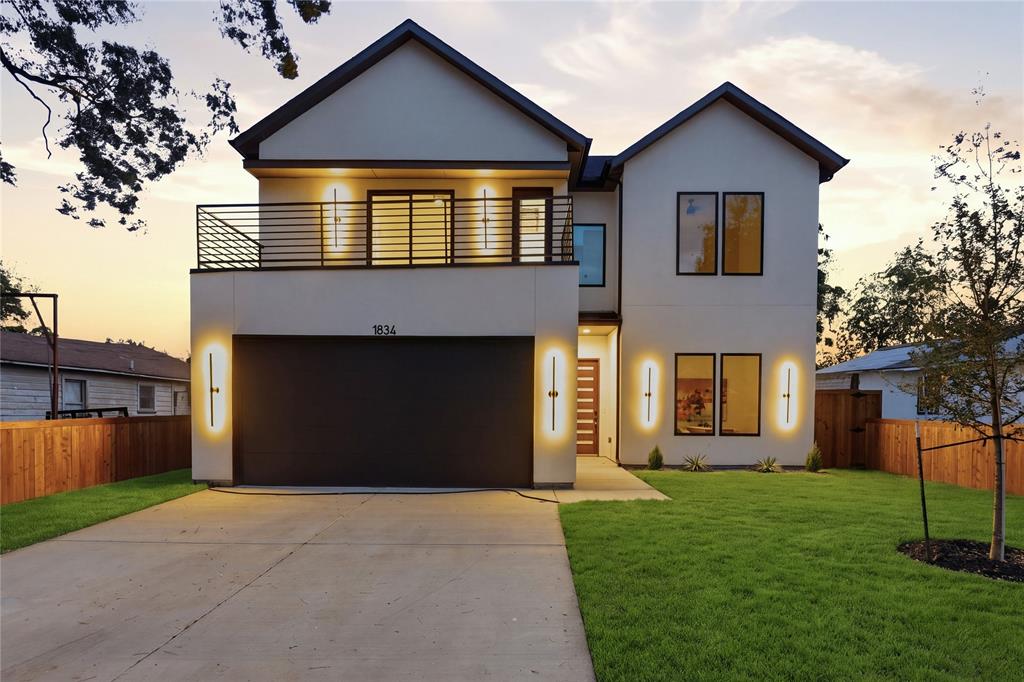 Two-story exterior featuring a smooth stucco facade, a second-level balcony with horizontal metal railing, tall vertical exterior wall sconces, multi-pane windows with dark trim, and a concrete driveway Two-story exterior featuring a smooth stucco facade, a second-level balcony with horizontal metal railing, tall vertical exterior wall sconces, multi-pane windows with dark trim, and a concrete driveway