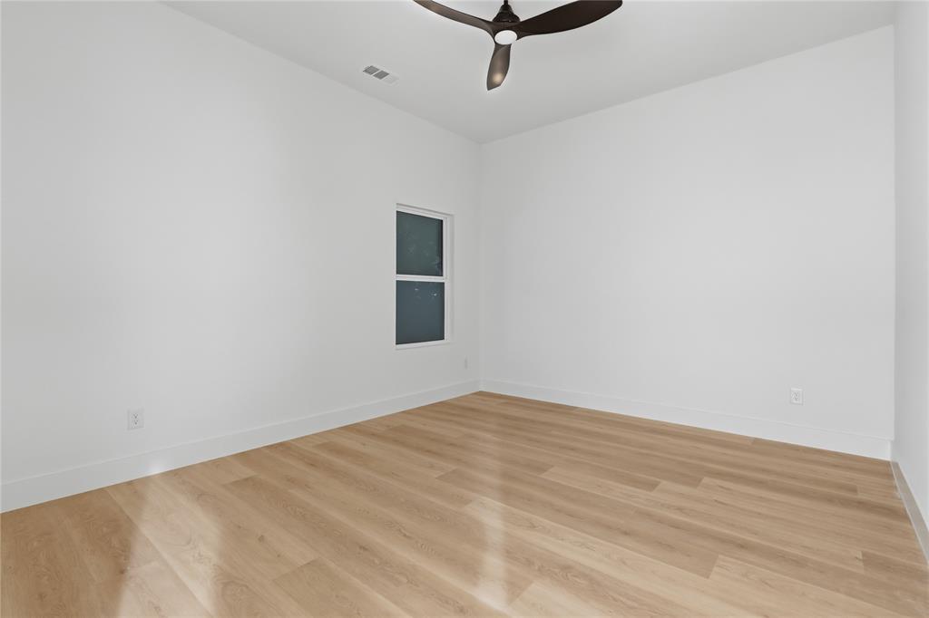Room featuring wood-finish flooring, neutral walls, and a multi-blade ceiling fan