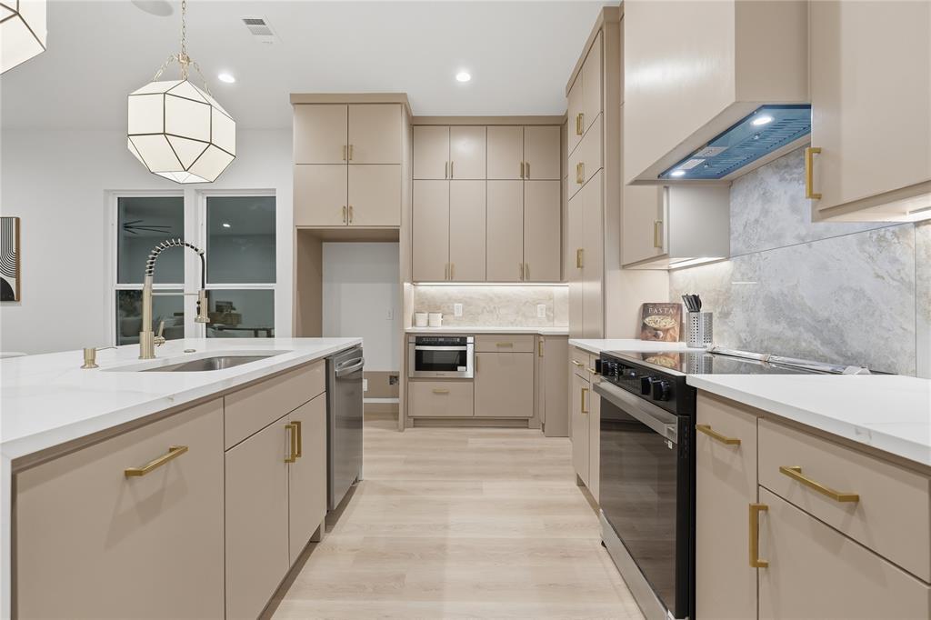 Kitchen featuring flat-panel cabinetry with gold-tone hardware, solid-surface countertops, stone-finish backsplash, built-in stainless steel appliances, and a geometric pendant light Kitchen featuring flat-panel cabinetry with gold-tone hardware, solid-surface countertops, stone-finish backsplash, built-in stainless steel appliances, and a geometric pendant light