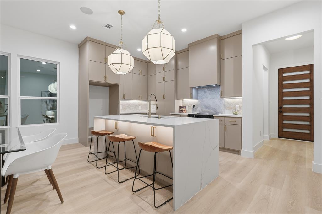 Kitchen featuring flat-panel cabinetry, quartz waterfall island, stone backsplash, geometric pendant lighting, and wood-finish flooring